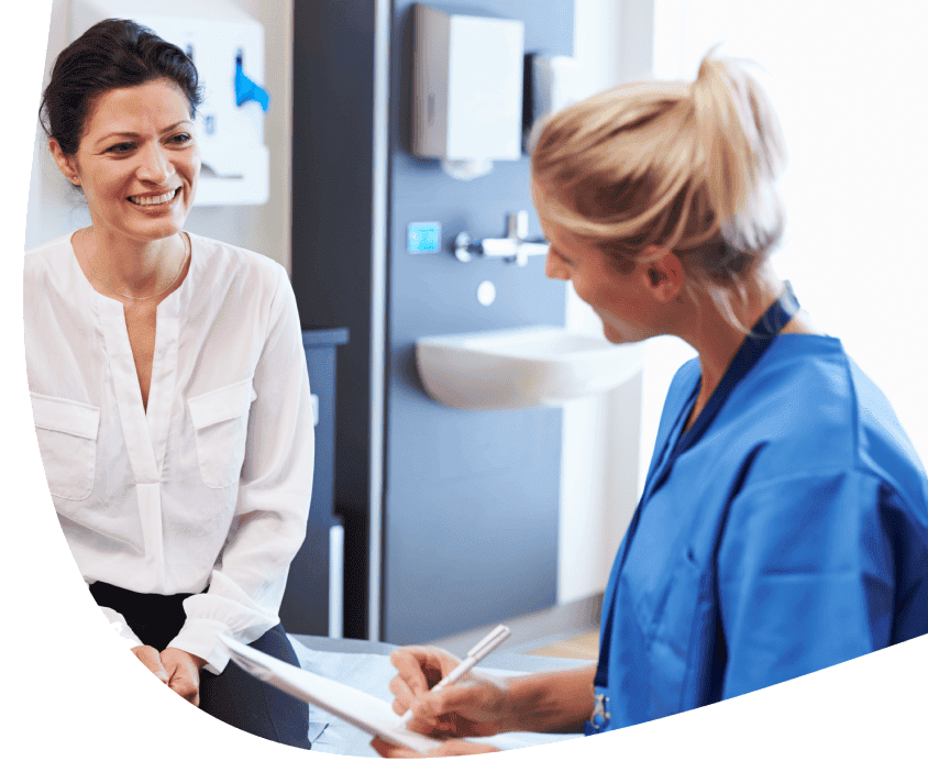 Žena v bielej blúzke sa rozpráva s osobou v modrej lekárskej uniforme, ktorá drží dokumenty.