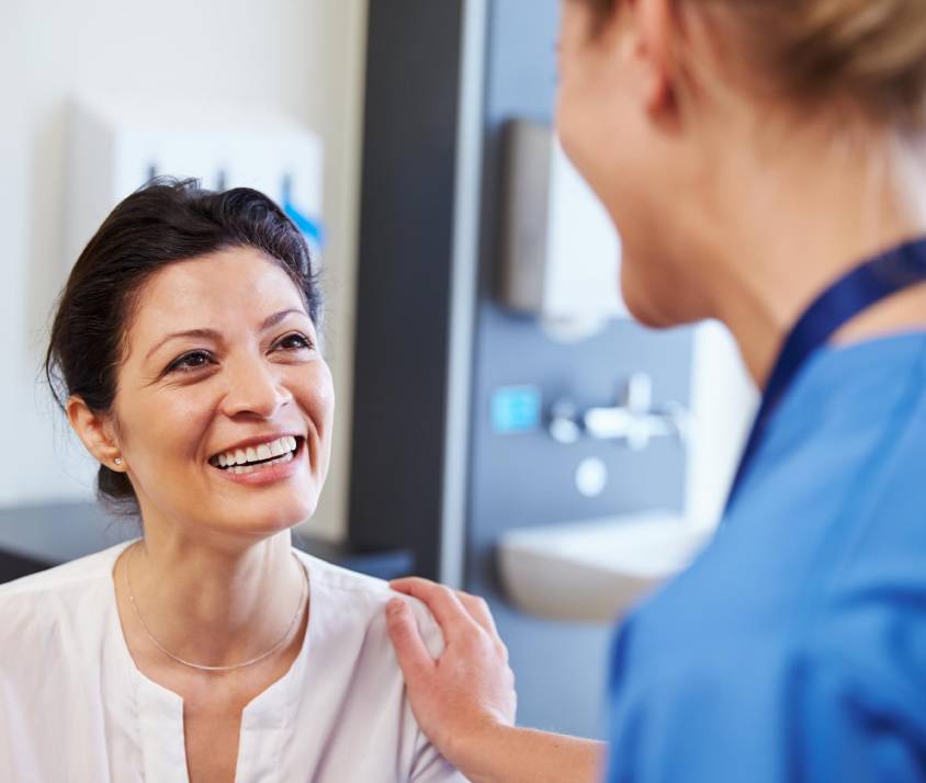 Usmievajúci sa pacient sa rozpráva so zdravotnou sestrou v ordinácii lekára.