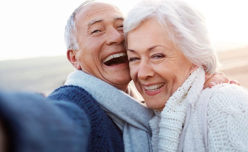 Starší pár sa smeje a objíma na pozadí otvorenej krajiny.